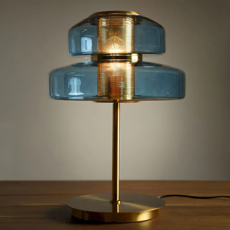Lampe à poser design en verre bleu et métal doré avec diffuseur central perforé. Un luminaire élégant et chaleureux pour salon ou chambre.