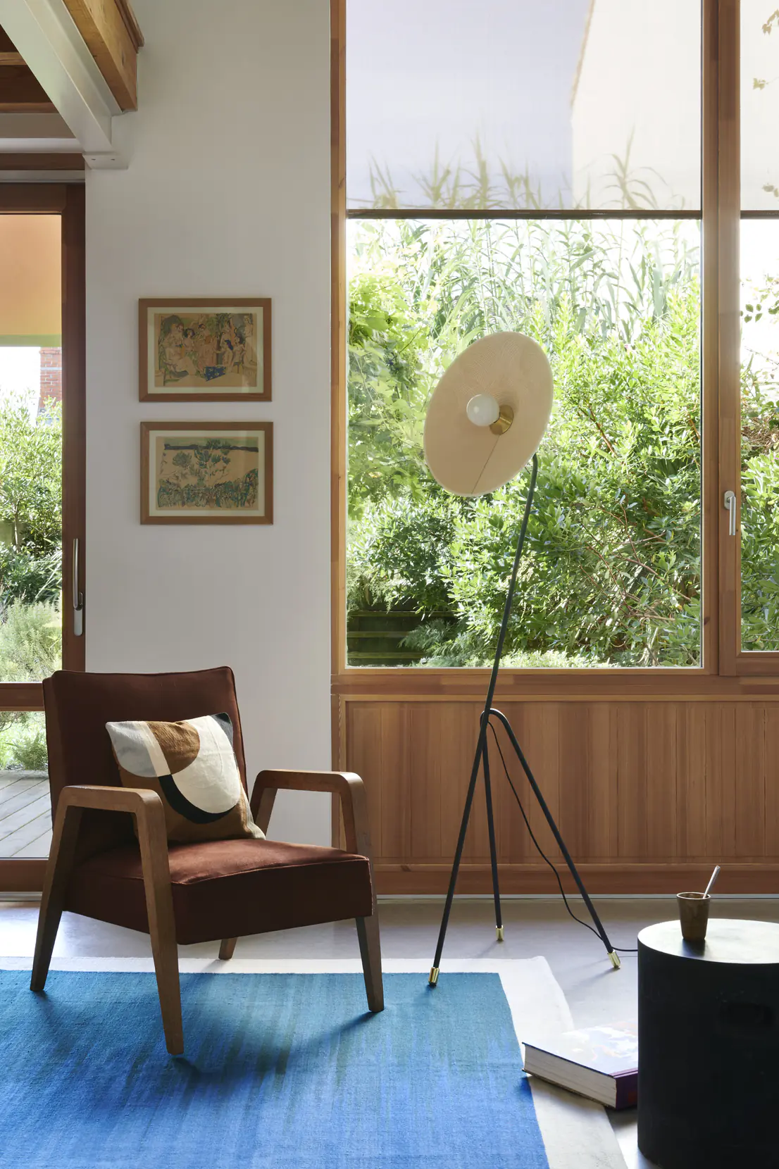 Lampadaire disque tissu retro allume a cote d'un fauteuil pres d'une fenêtre.