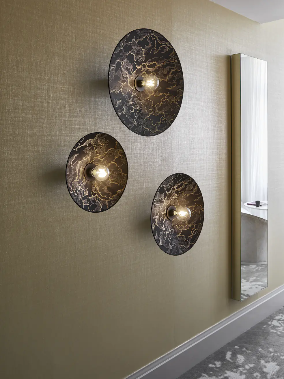 Composition de trois appliques disque en tissu allumees sur un mur dore.