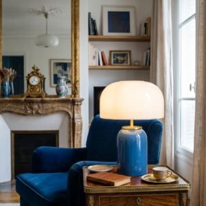 Lampe champignon en verre bleu allumee sur un buffet en bois.